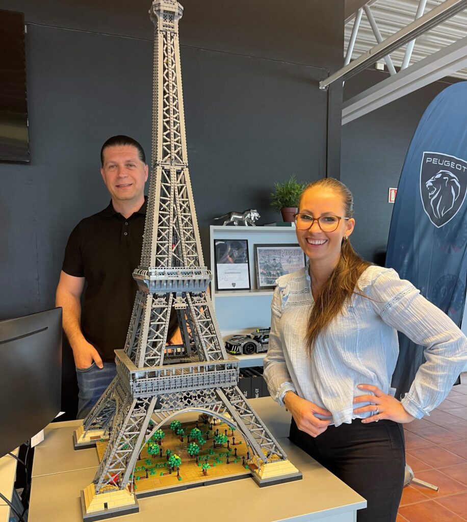 Mirzet Mahmuljin og Mona Sagen står smilende ved en stor LEGO-modell av Eiffeltårnet, utstilt hos Kongsvinger Bilsenter under Fransk dager i juni.