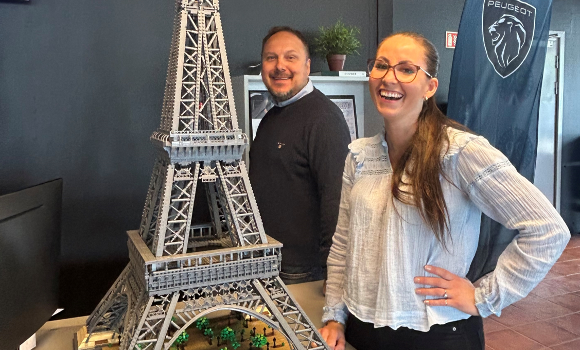 Mona Sagen og Stig Strømstad smiler ved siden av en imponerende LEGO-modell av Eiffeltårnet, utstilt inne hos Kongsvinger Bilsenter i forbindelse med Fransk junifest.
