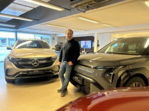 Bruktbilutstilling hos Kongsvinger Bilsenter med Mercedes-Benz EQA og KIA, og selger som står mellom bilene i showroom.